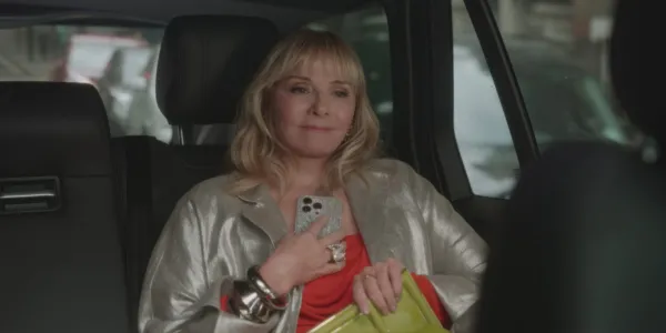 Kim Cattrall como Samatha Jones em And Just Like That 2ª temporada, sentada no banco de trás de um carro, segurando o telefone e a bolsa.