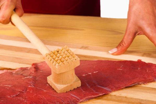 femme attendrissant la viande avec un maillet en bois sur une planche à découper