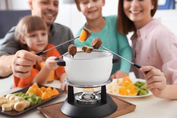 famille souriante de quatre fruits plongeant dans une fondue au chocolat