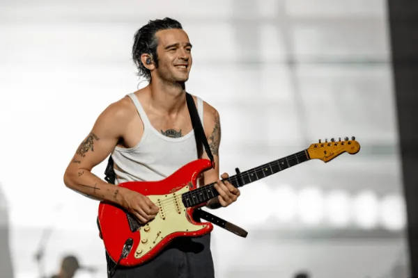 Matty Healy vestindo uma blusa branca e segurando uma guitarra elétrica