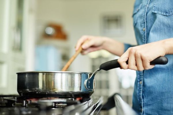La sezione centrale sotto visualizza l'immagine della donna che cucina il cibo in padella. L'utensile è posto sul fornello a gas. La femmina sta mescolando il piatto in padella. Sta preparando il cibo nella cucina domestica.