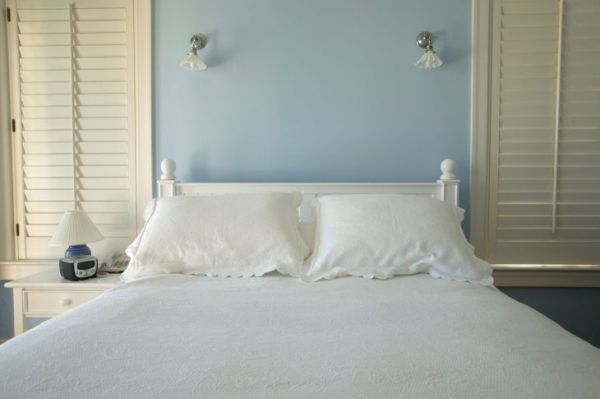 Mavi divarları və ağ çarpayısı olan yataq otağı.
