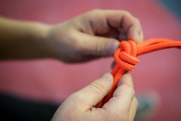 corde d'escalade orange vif avec des nœuds dans les mains d'un enfant en t-shirt vert