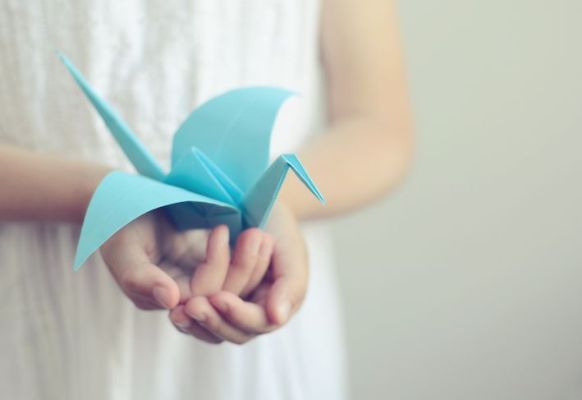 Bambina che tiene in mano un uccello origami blu