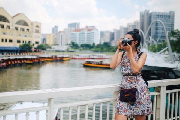 Obrázek mladé módní bruneta ženy. Odpočívá po dni dlouhých procházek, nosí ležérní, ale módní šaty, užívá si krásný den v rušných ulicích Singapuru, fotí svým retro bezzrcadlovkou nebo skutečnou 35mm analogovou zrcadlovkou.