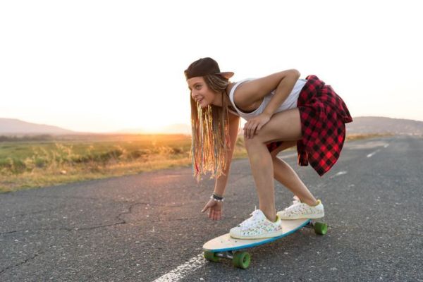 Krásná mladá žena skateboarding na venkovské silnici, při západu slunce.