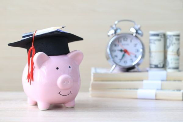 Chapeau de graduation sur tirelire bleue avec pile de pièces d'argent sur fond en bois, économiser de l'argent pour le concept d'éducation