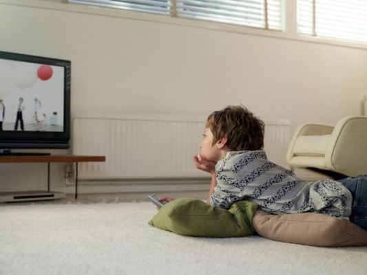 ბიჭი სახლში იატაკზე იწვა და ტელევიზორს უყურებს