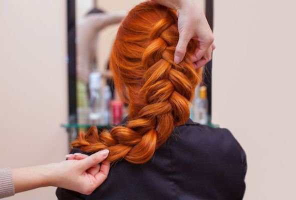 美丽的红发女孩，长发，美发师在美容院编织法式辫子