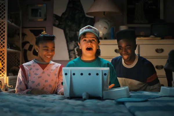Priah Ferguson, Gaten Matarazzo e Caleb McLaughlin se reúnem em torno de uma tela na 4ª temporada de Stranger Things