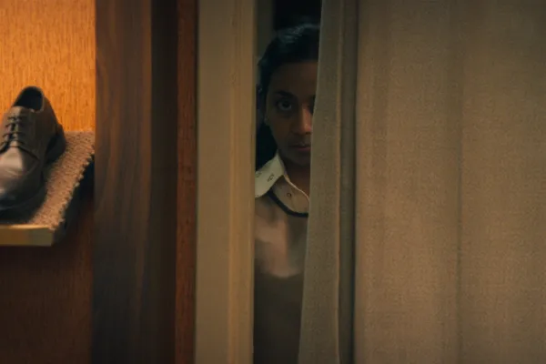 Anjana Vasan espiando por uma fresta na porta